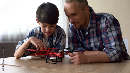 Curious father and little son examining new quadrocopter model at home, fun