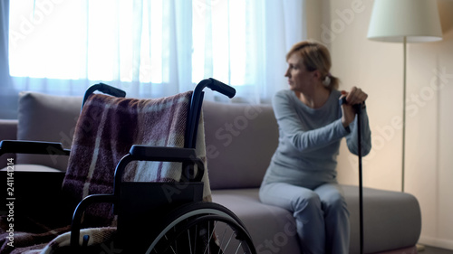 Photography Disabled lady sitting on sofa and looking in window, empty wheelchair in room