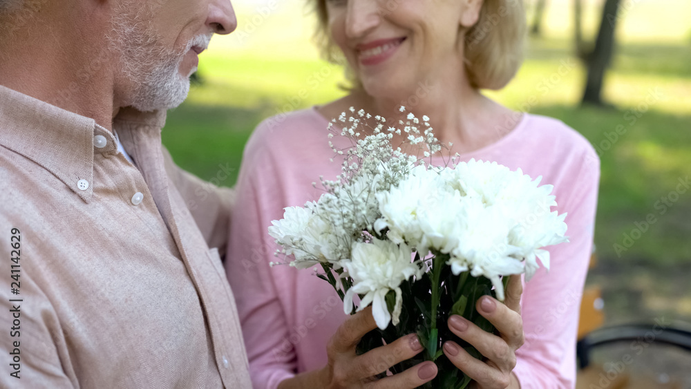 Pretty aged woman taking flower present from man, romantic date in park, love Pretty aged woman taking flower present from man, romantic date in park, love