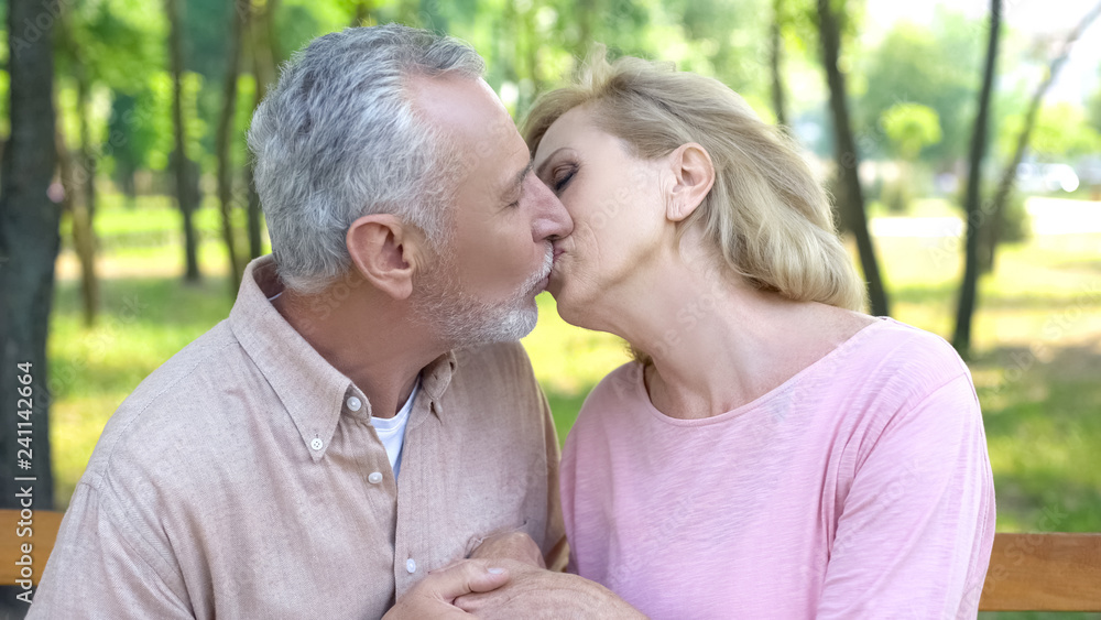 Mature couple kissing in park, happy marriage, strong love and care for all life