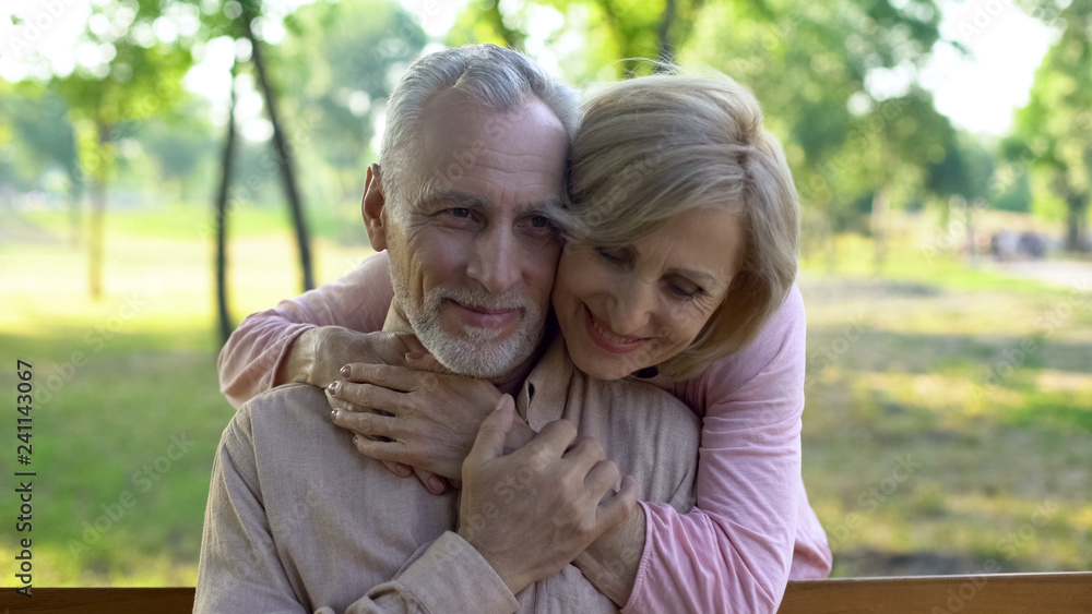 Senior woman hugging husband behind, romantic meeting in park, flirt and fun Senior woman hugging husband behind, romantic meeting in park, flirt and fun