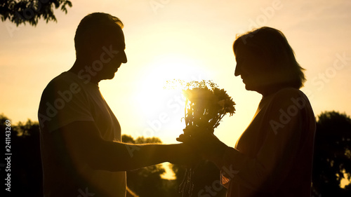 Caring man presenting flowers to woman at sunset, wedding anniversary, love
