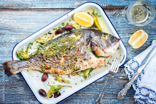 Fresh Greek barbecue gilthead seabream with peperoni and Kalamata olives as top view in a white skillet photo