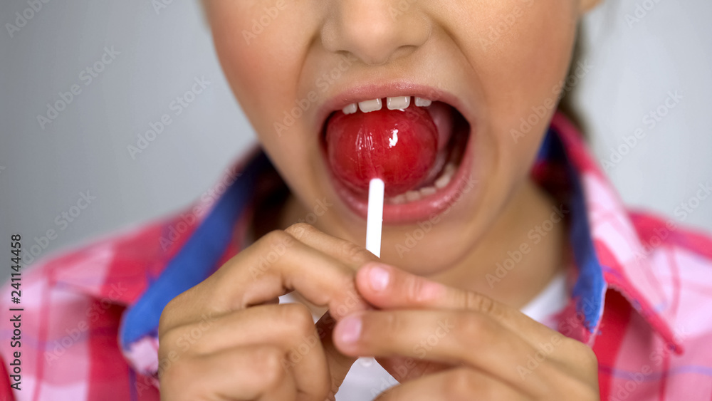 Childish girl biting sweet lollipop, effect of sugar on teeth, diabetics risk Childish girl biting sweet lollipop, effect of sugar on teeth, diabetics risk