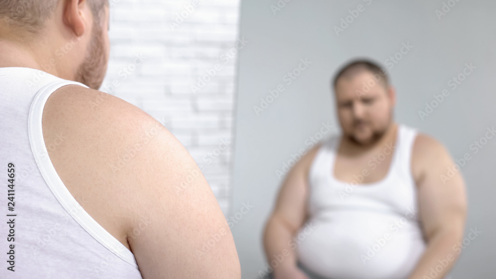 Obese man looking at his mirror reflection, overweight problem and insecurities Obese man looking at his mirror reflection, overweight problem and insecurities