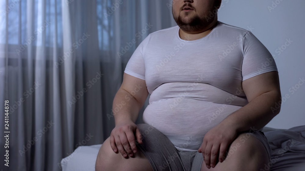 Fat man sitting on bed, weight gain due to sedentary lifestyle