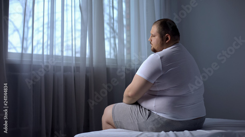 Картината върху платно Depressed fat man sitting on bed at home, worried about overweight, insecurities
