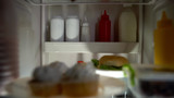 Closeup of junk food inside fridge, unhealthy nutrition, high calorie meal