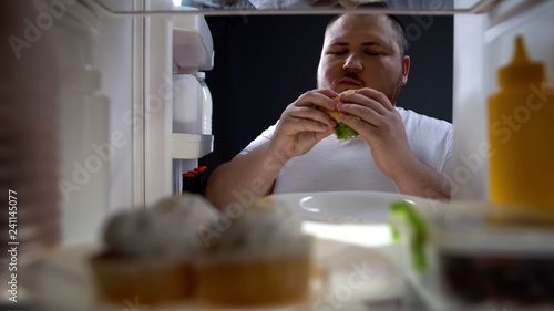 Obese man eating cheeseburger with pleasure, diet failure, unhealthy lifestyle