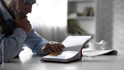Elderly male looking at photos in album at kitchen table, pleasant memories