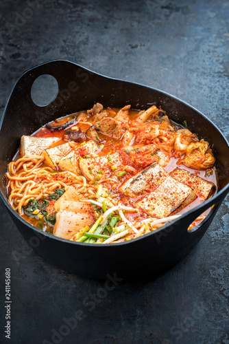 Traditional Korean kimchi jjigae with grilled pork belly and ramen as closeup in a modern design Japanese cast-iron roasting dish