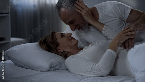 Elderly couple caressing in bed, man kissing woman hand, love in marriage