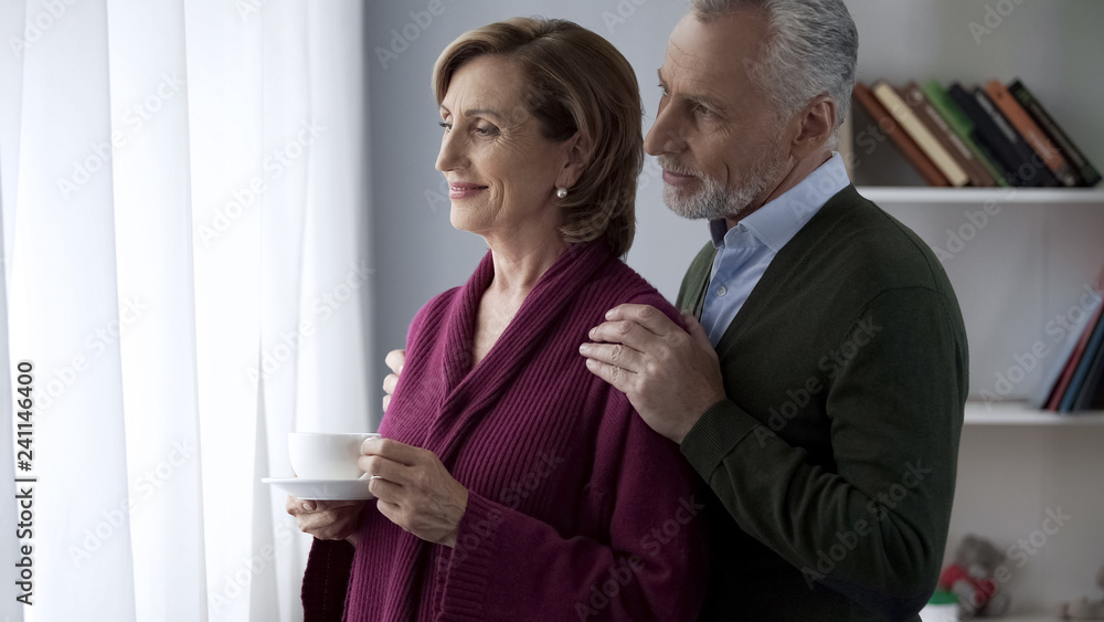 Senior couple looking in window, male hugging lady shoulders from behind, family Senior couple looking in window, male hugging lady shoulders from behind, family
