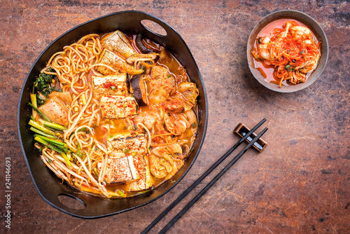 Traditional Korean kimchi jjigae with grilled pork belly and ramen as top view in a modern design Japanese cast-iron roasting dish
