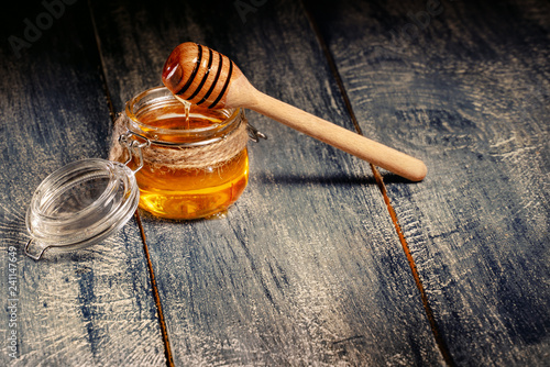 Honey in jar with wooden dipper on dark wooden table