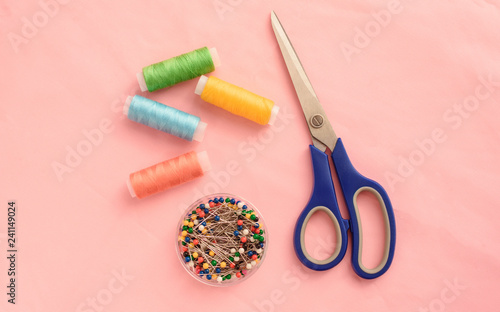Small sewing kit, threads, pins in container and scissors on pink background
