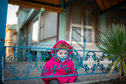 Bambina sorridente con giubbotto fucsia alla moda su ringhiera blu e palma verde photo