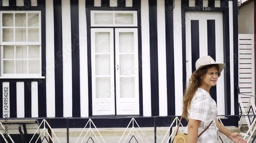 Young woman pass by camera at background colorful house wall. Girl moving funny walk and looking at camera with funny face. Costa Nova, Portugal
