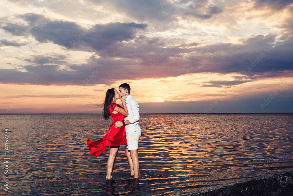 young couple in love kisses standing in the sea against the backdrop of a beautiful sunset. young couple in love kisses standing in the sea against the backdrop of a beautiful sunset.