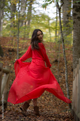 Black haired and green eyed woman in red dress in the forest.