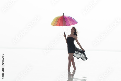 Woman holding colorful umbrella and walking on the salt lake. Sunrise sea and woman with umbrella in hand 