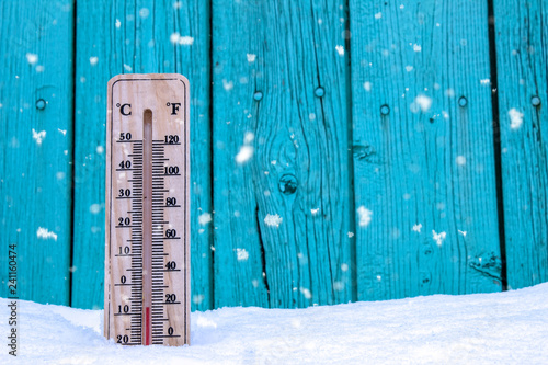 Wooden thermometer on a background of green boards and white snow