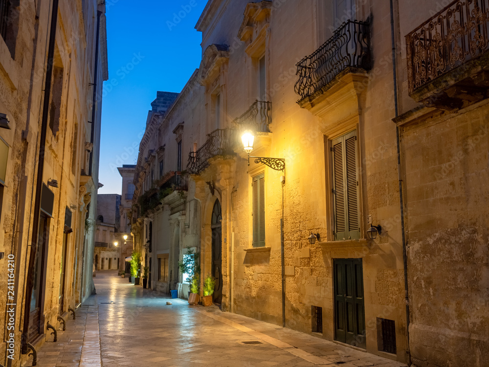 Traditional historic architecture in Lecce city, illuminated street and houses at dusk in Italy
