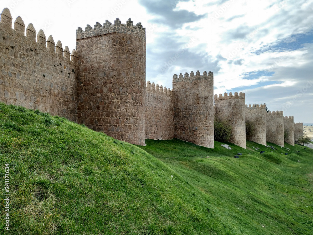 The wall of Avila, Spain. The stone wall with its turrets behind a green lawn.