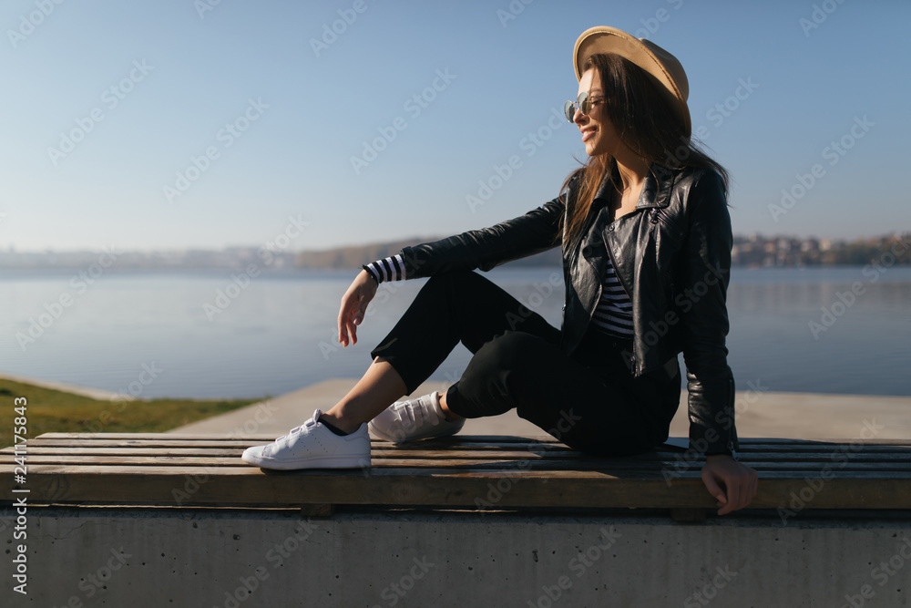 Side portrait of young woman with fanky hat sitting on the bench on pier of city lake Side portrait of young woman with fanky hat sitting on the bench on pier of city lake