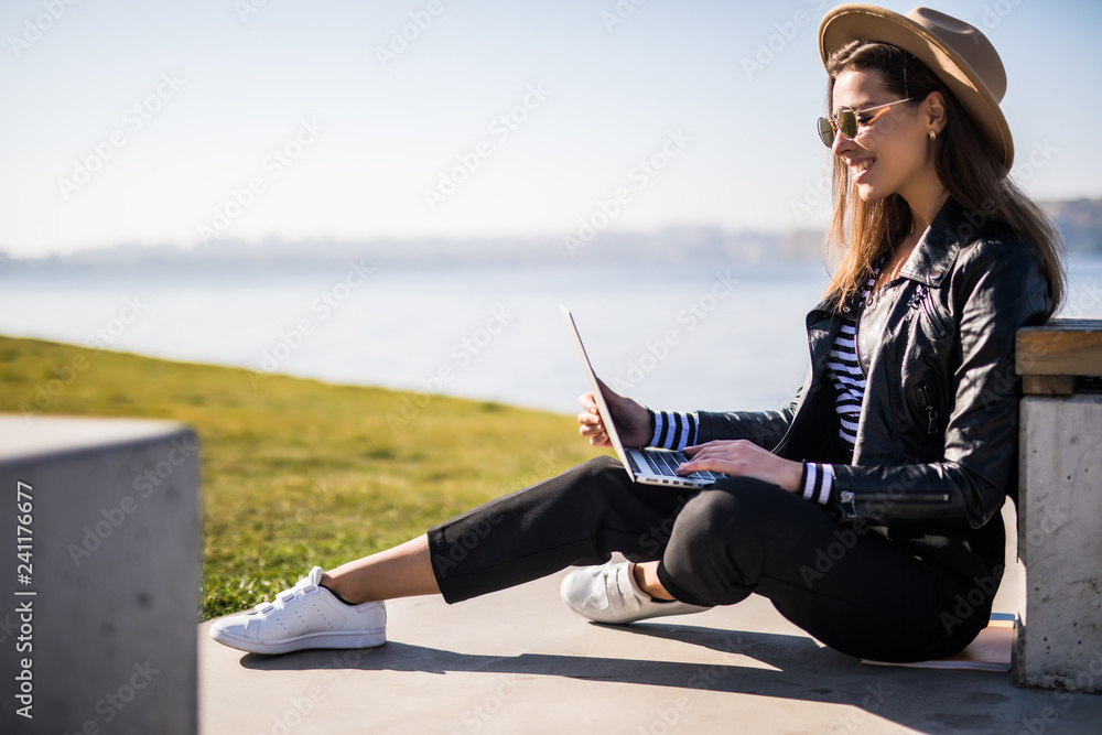 Young pretty woman sitting on the bench and use wifi with her laptop in urban city space