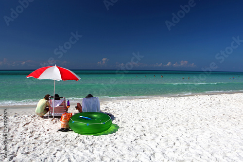 A family sits under an umbrella on a sandy beach in the Florida panhandle.