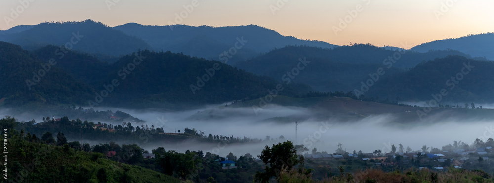 The village is surrounded by mountains at sunrise time with foggy.
