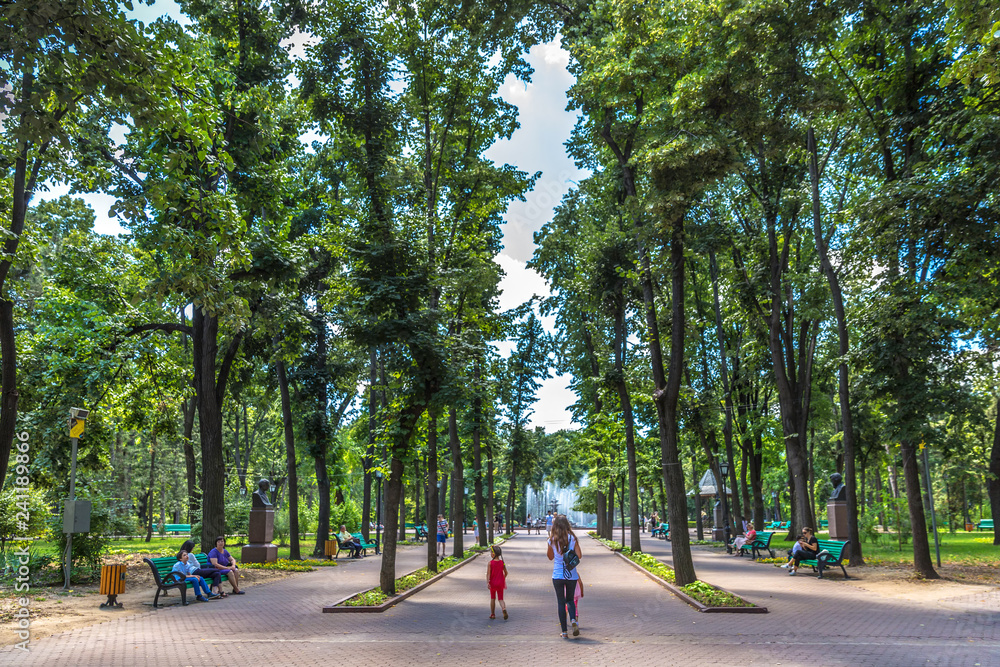 Chisinau, Moldavia - July 4th 2018 - Locals and tourists walking through a open air park with high green trees in a summer european day