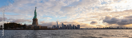 Panoramic view of the Statue of Liberty and Downtown Manhattan in the background during a vibrant cloudy sunrise. Taken in Jersey City, New Jersey, United States. © edb3_16