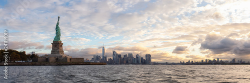 Panoramic view of the Statue of Liberty and Downtown Manhattan in the background during a vibrant cloudy sunrise. Taken in Jersey City  New Jersey  United States.