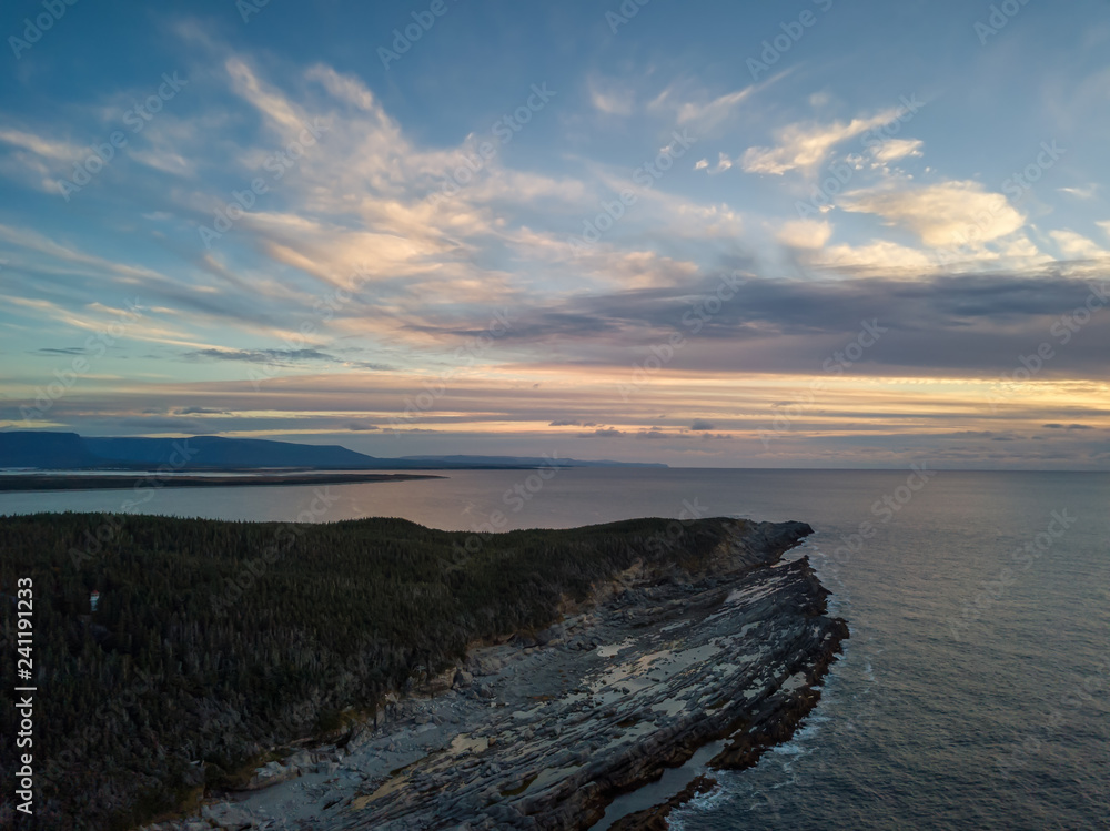 Aerial view of a rocky shore on the Atlantic Ocean Coast during a vibrant sunny sunset. Taken in Cow Head, Newfoundland, Canada.