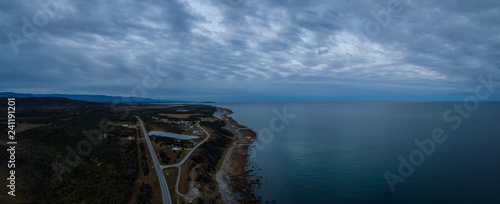Aerial panoramic view of a scenic road near the Atlantic Ocean Coast during a dramatic cloudy sunrise. Taken in Newfoundland, Canada.
