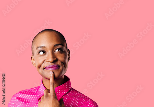 Obraz na plátně Portrait of a young woman in pink shirt with finger on mouth looking up thinking