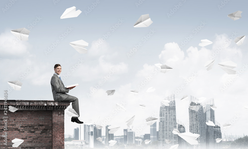 Man on roof edge reading book and cityscape at background Man on roof edge reading book and cityscape at background