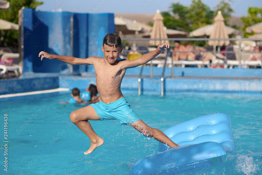 Cute European boy is diving from the inflatable blue floater into the hotel’s swimming pool. He is enjoying his summer vacations.