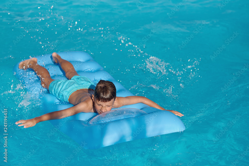  Caucasian boy  is  swimming  on blue  inflatable mattress at hotel swimming pool. He is enjoying his summer vacations. Copy space.