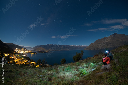 Young couple climbs up a hill to look at Queenstown, New zealand at night. Night scene of queenstown, New Zealand. Young traveler enjoying beautiful night view of city.