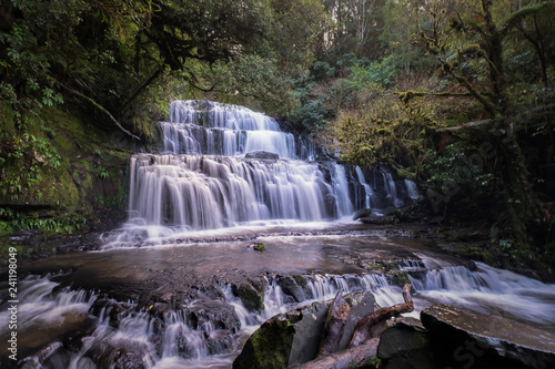 Fototapeta Naklejka Na Ścianę i Meble -  This is the Purakaunui Falls in New Zealand. A waterfall is a place where water flows over a vertical drop or a series of steep drops in the course of a stream or river.