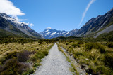 A long straight gravel road that leads to the famous breathtaking snow mountain in Mount Cook, New Zealand. The landscape is epic. There are snow mountain, glacier, alpine, rivers and valley.