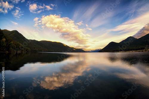A peaceful and calming image of a lake. The water is smooth and clear. It reflects the clouds and the sky above. It was sunrise therefore the clouds are yellow and warm. The image is beautiful. © Skyimages