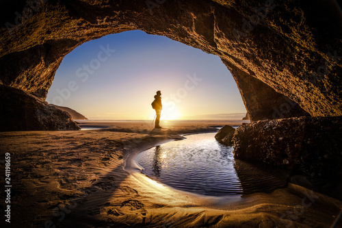 People explores a cave during sunrise at Wharariki Beach New Zealand