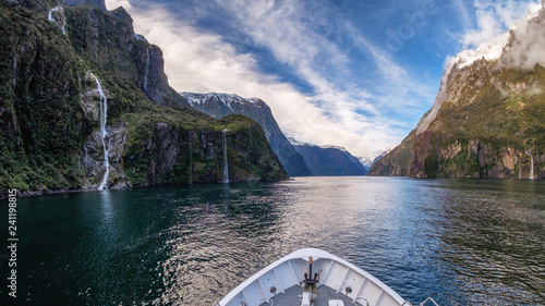 In Milford Sound cruise, one experience the spray of a waterfall close to sheer rock faces. A popular tourist destination and natural landscape in New Zealand. This view is breathtaking and iconic.