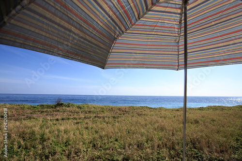 A colorful umbrella by the coast. It was a sunny beautiful day and it is perfect for a walk along the coast. The view is beautiful. There are high cliff. This image is suitable for background use.