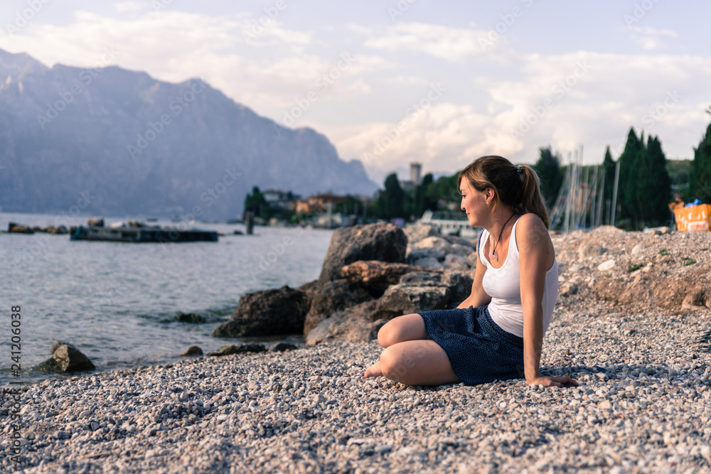 Beautiful young woman is sitting on the pebble beach and enjoying the view, vacation Beautiful young woman is sitting on the pebble beach and enjoying the view, vacation