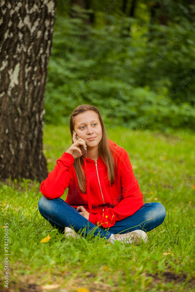 modern teenager girl sitting on the grass in the park with a smartphone in her hands